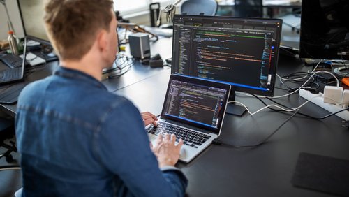 Ein Programmierer sitzt vor einem Laptop und schreibt Code. 