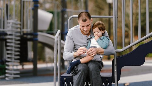 Nachdenklicher Vater legt seinem kleinen Sohn im Park einen Verband auf das Knie