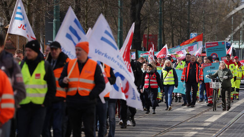 Mit Fahnen ausgestattete Streikende ziehen bei einem Streik durch eine Straße.