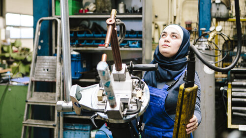 Young female trainee transports a welding point pliers with a crane in a workshop
