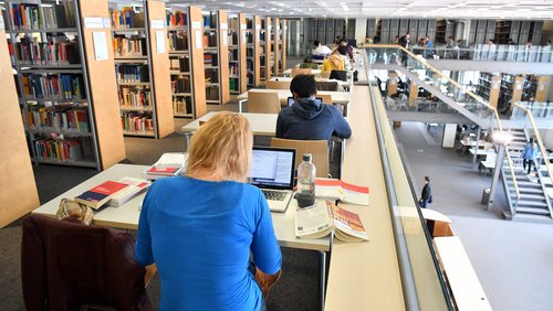 Studenten sitzen in einer Bibliothek an Schreibtischen.