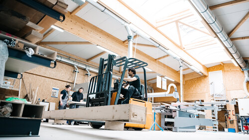 Arbeiter mit Gabelstapler in der Schreinerei-Fertigungshalle vor dem Lagerregal 