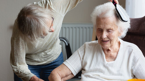 Woman, more than 60 years old, combing the hair of a senior woman in her nineties with a brush, the old woman enjoys the care she is getting from the younger woman