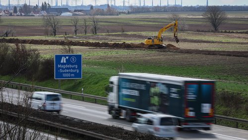 Blick auf ein Feld, auf dem ein Bagger arbeitet. Im Vorderbrund ist eine Autobahn zu sehen, ein Schild verweist auf die Ausfahrt Magedeburg-Sudenberg.