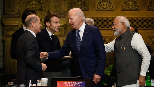 Olaf Scholz, Emmanuel Macron, Joe Biden und Narendra Modi begrüßen sich in einem holzgetäfelten Konferenzraum.