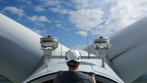 Ein Arbeiter prüft die Rotorblätter einer Windkraftanlage.