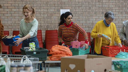 Gruppe von Freiwilligen, die Lebensmittelspenden auf Tische einer Lebensmittelbank organisieren. Sie arbeiten zusammen und richten Teile des Raumes in einer Kirche ein. Gruppe von Freiwilligen, die Lebensmittelspenden auf Tische einer Lebensmittelbank organisieren. Sie arbeiten zusammen und richten Teile des Raumes in einer Kirche ein.