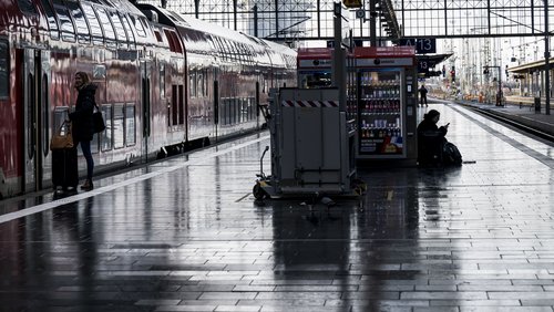 Ein leerer Bahnsteig an einem deutschen Bahnhof. Ein Mensch steigt in eine Regionalbahn ein, ein anderer sitzt auf dem Boden.