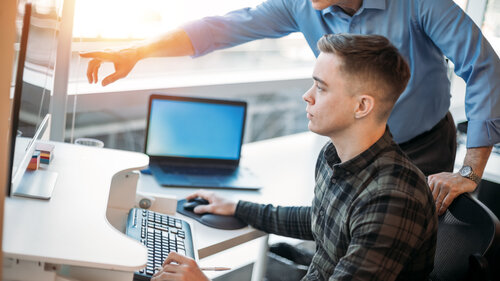 Colleague mentoring younger associate in business office while pointing at data on computer monitor