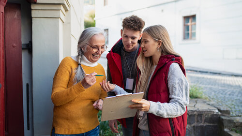 Young door to door volunteers talking to senior woman and taking a survey at her front door. Young door to door volunteers talking to senior woman and taking a survey at her front door.