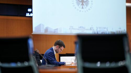 Marco Buschmann sitzt im Parlament vor einer großen Leinwand