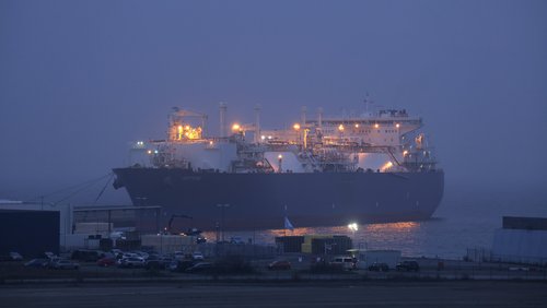 Ein beleuchteter Gastanker fährt im Morgengrauen in einen Hafen ein.