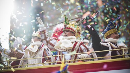 Kinderdreigestirn wirft Kamelle von einem bunten Umzugswagen und lächeln 
