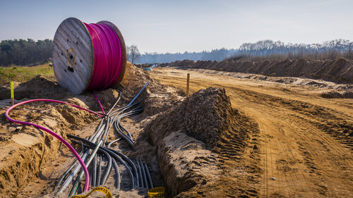 Kabel werden von einer Trommel im Boden auf einer Baustelle verlegt.