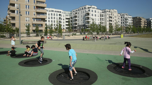 Kinder hüpfen auf einem Trampolin auf einem Spielplatz in einer Berliner Neubausiedlung mit vielen Wohnungen