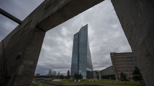 Blick durch ein Mauerloch auf den Wolkenkratzer der EZB in Frankfurt. Im Vordergrund ein Park und eine Joggerin.