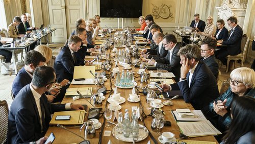 An einem langen Tisch sitzen die Ministerinnen und Minister der Bundeskabinetts sowie IW-Direktor Michael Hüther.
