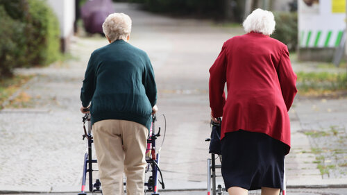 Zwei Seniorinnen schieben ihre Rollatoren nebeneinander her.
