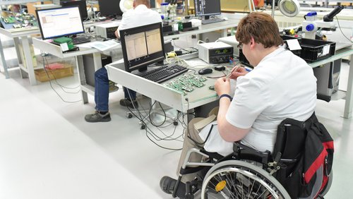 Ein Mitarbeiter im Rollstuhl montiert elektronische Komponenten. Oftmals sind Menschen mit Behinderungen sehr gut qualifiziert. 