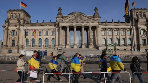 Ein Gruppe von Menschen ist in Ukraine-Flaggen eingewickelt und geht das Reichstagsgebäude entlang.