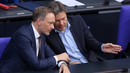 Christian Lindner und Robert Habeck stecken am Regierungstisch im Deutschen Bundestag die Köpfe zusammen und tauschen sich aus. Robert Habeck spricht, und gestikuliert nach rechts, Lindner hört zu.