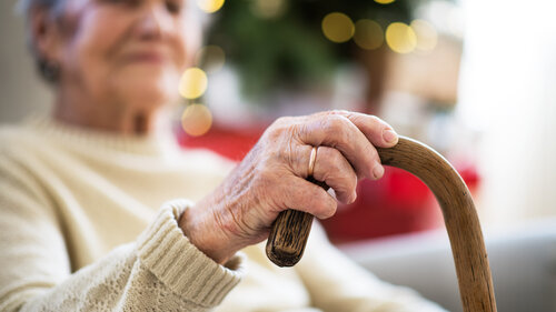 A close-up of a senior woman holding a walking stick at home at Christmas time.