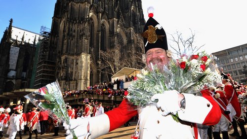 Ein Vertreter der Karnevalsgesellschaft Rote Funken verteilt vor dem Dom Strüßje.